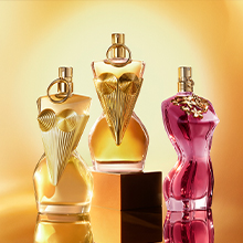 Drei Jean Paul Gaultier Parfumflakons in femininer Silhouette mit kunstvoll vergoldeten Details, stilvoll inszeniert vor goldenem Hintergrund.
