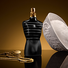 Jean Paul Gaultier Le Male Le Parfum in schwarzer Flasche mit goldener Kappe und weißen Streifen, begleitet von weißer Matrosenmütze und goldener Kette.