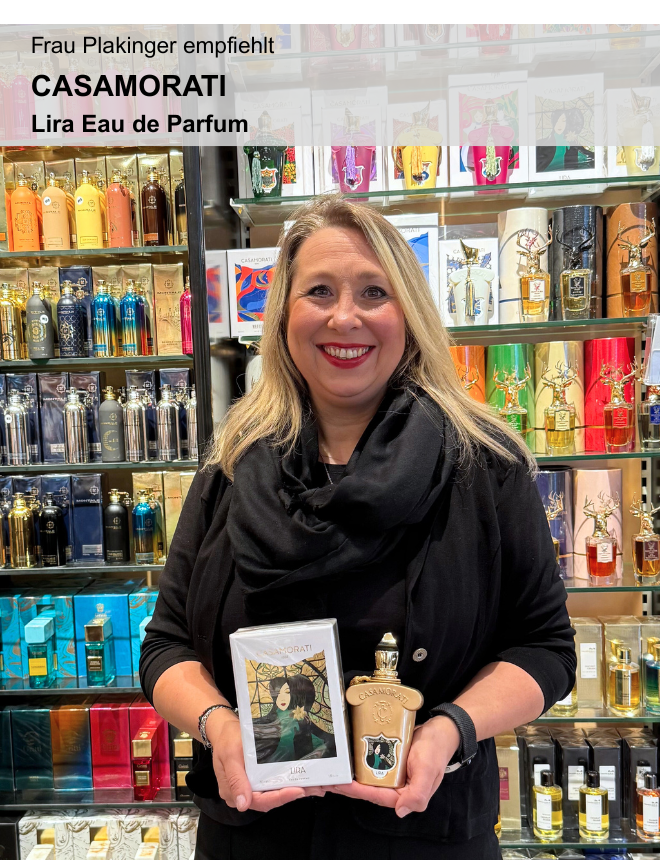 Verkäuferin Frau Plakinger empfiehlt Casamorati Lira Eau de Parfum mit Verpackung vor Duftregal im Fachgeschäft