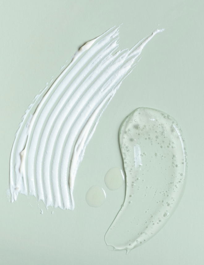Weiße Cremestreifen und durchsichtiges Serum auf mintgrünem Hintergrund, Artikelbild Inhaltsstoffe in Pflegeprodukten