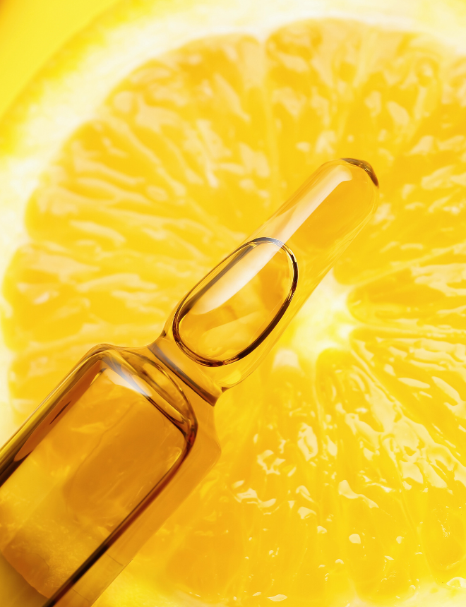 Goldene Vitamin-C-Ampulle liegt auf aufgeschnittener Orange, Artikelbild Inhaltsstoffe in Pflegeprodukten