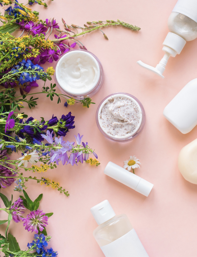 Naturkosmetik-Produkte wie Creme, Peeling und Lippenpflege umgeben von bunten Wildblumen, Artikelbild Naturkosmetik