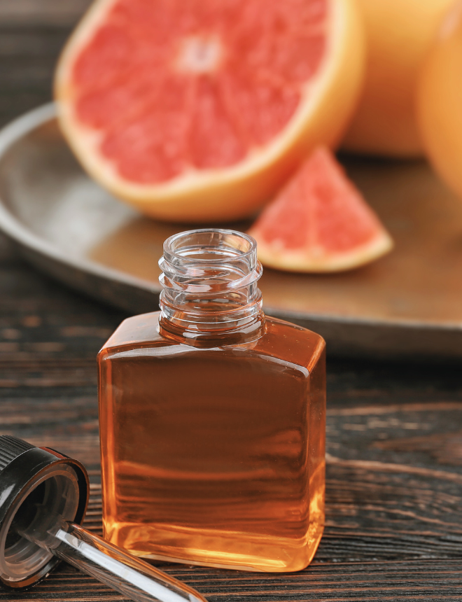 Parfümflacon mit bernsteinfarbenem Duft neben aufgeschnittener Grapefruit, Herbstdüfte fruchtig