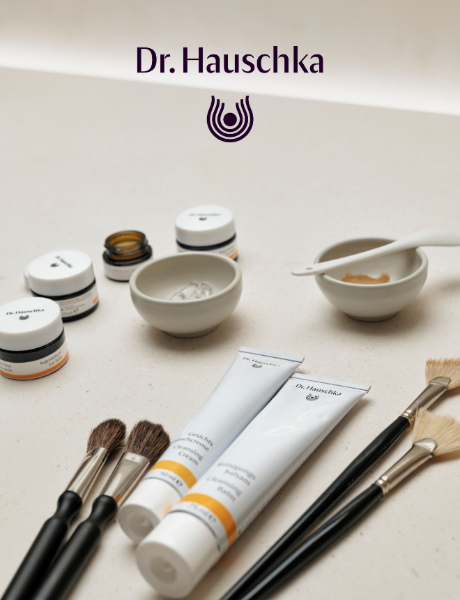Dr. Hauschka Logo mit Reinigungscreme, Cremebalsam und Naturkosmetik-Pinseln auf beigem Untergrund