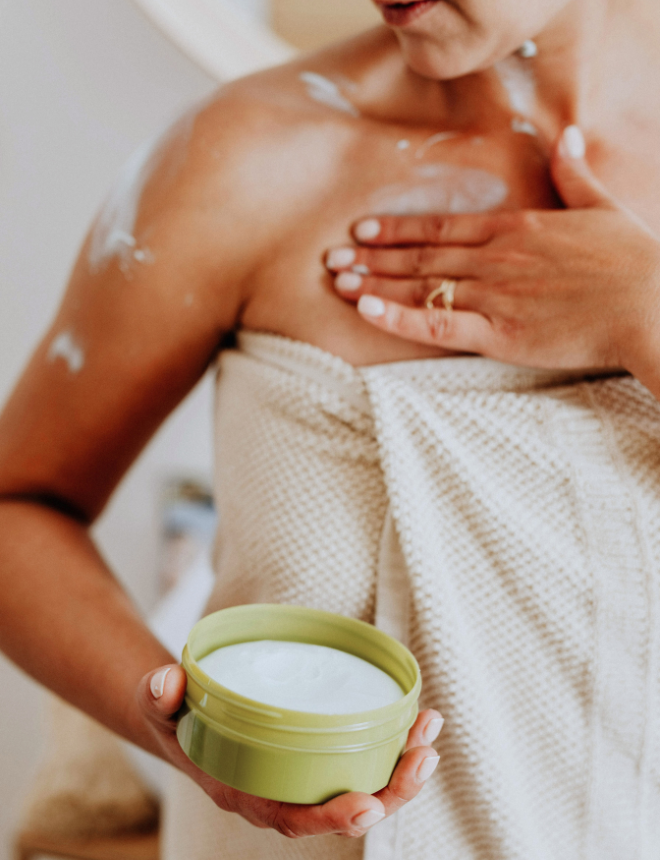 koerperpflege-660x860.png Frau in Handtuch trägt Naturkosmetik-Körpercreme aus grünem Tiegel auf Schulter und Dekolleté auf