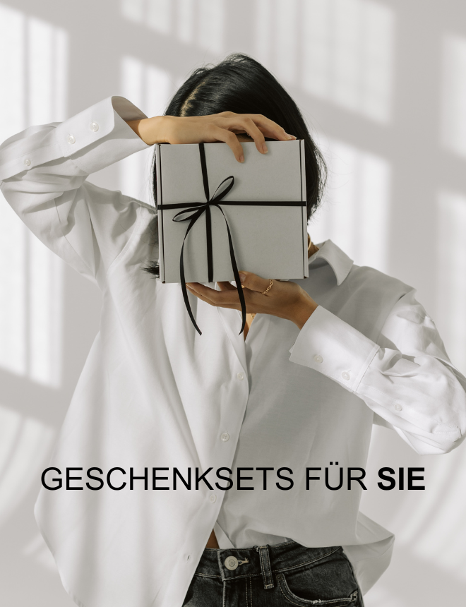 Geschenksets für Sie – Frau hält verschenkte Geschenkbox mit Schleife vor dem Gesicht