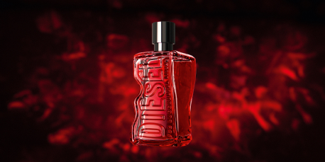 Roter Parfumflakon von Diesel in muskulöser Form mit geprägtem Logo auf der Vorderseite. Der Hintergrund ist dynamisch in verschiedenen Rottönen gestaltet und erzeugt eine intensive, energiegeladene Atmosphäre. Der schwarze Verschluss steht im Kontrast zur transparenten roten Glasflasche.