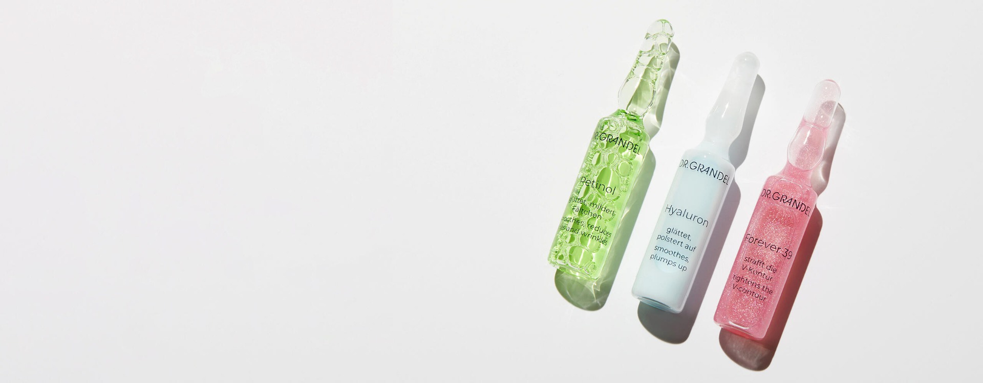 Drei Dr. Grandel Ampullen mit Pflegekonzentrat: grüne Retinol-Ampulle, blaue Hyaluron-Ampulle und rosa Forever 39-Ampulle auf weißem Hintergrund mit Schattenwurf.