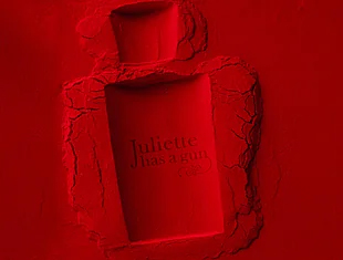 Roter Hintergrund mit eingedrücktem Abdruck eines Parfümflakons der Marke ‚Juliette has a gun‘. Die Konturen des Flakons und der Schriftzug sind im plastischen Relief sichtbar.