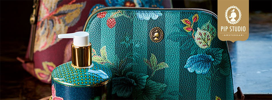 Stimmungsvolle Nahaufnahme von Produkten der Marke Pip Studio Amsterdam: Im Vordergrund ein türkisgrünes Kosmetiktäschchen mit floralem Muster und goldener Verzierung, daneben ein passender Seifen- oder Lotion-Spender mit goldener Pumpe. Im Hintergrund ein weiteres Täschchen in Rottönen. Rechts oben das Pip Studio-Logo auf goldenem Hintergrund.